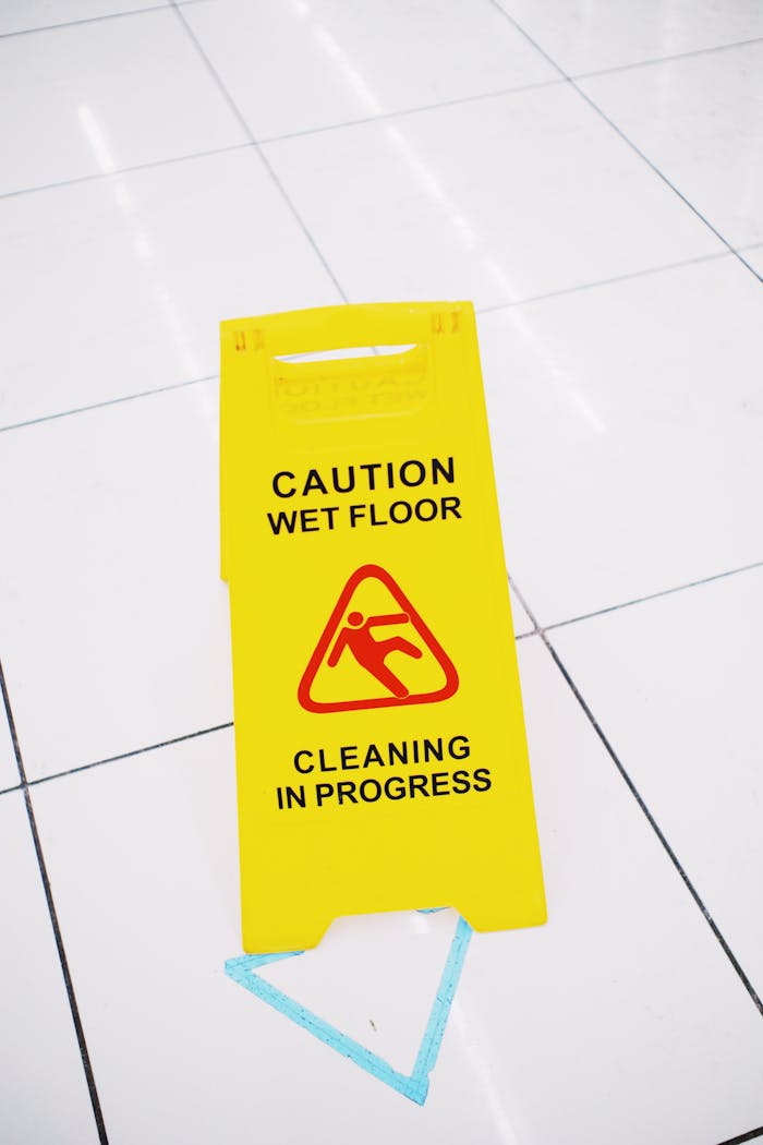 who-we-are Bright yellow caution wet floor sign on white tiled floor indoors.